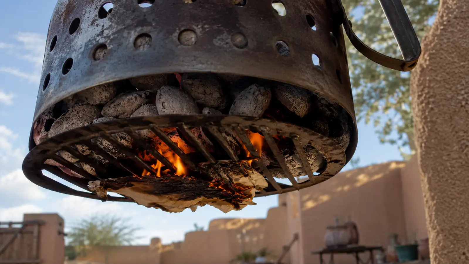 A single sheet of crumpled newspaper burning under the bottom grate of a charcoal chimney starter loaded with briquettes