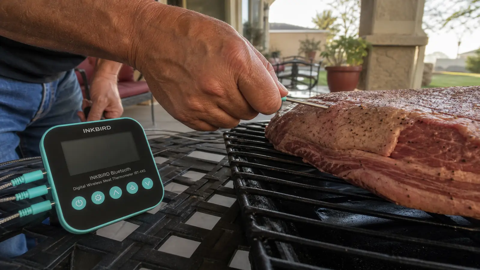 A man's hand inserting a probe with a colored silicone tip into the thick end of a brisket flat on a smoker grate