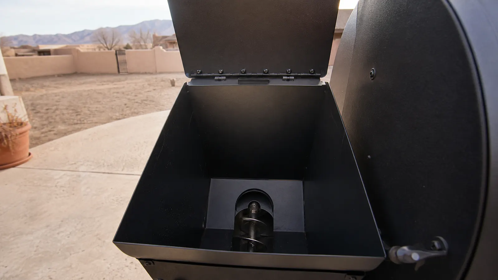 A pellet grill hopper lid propped open showing the auger screw at the bottom, empty and clean