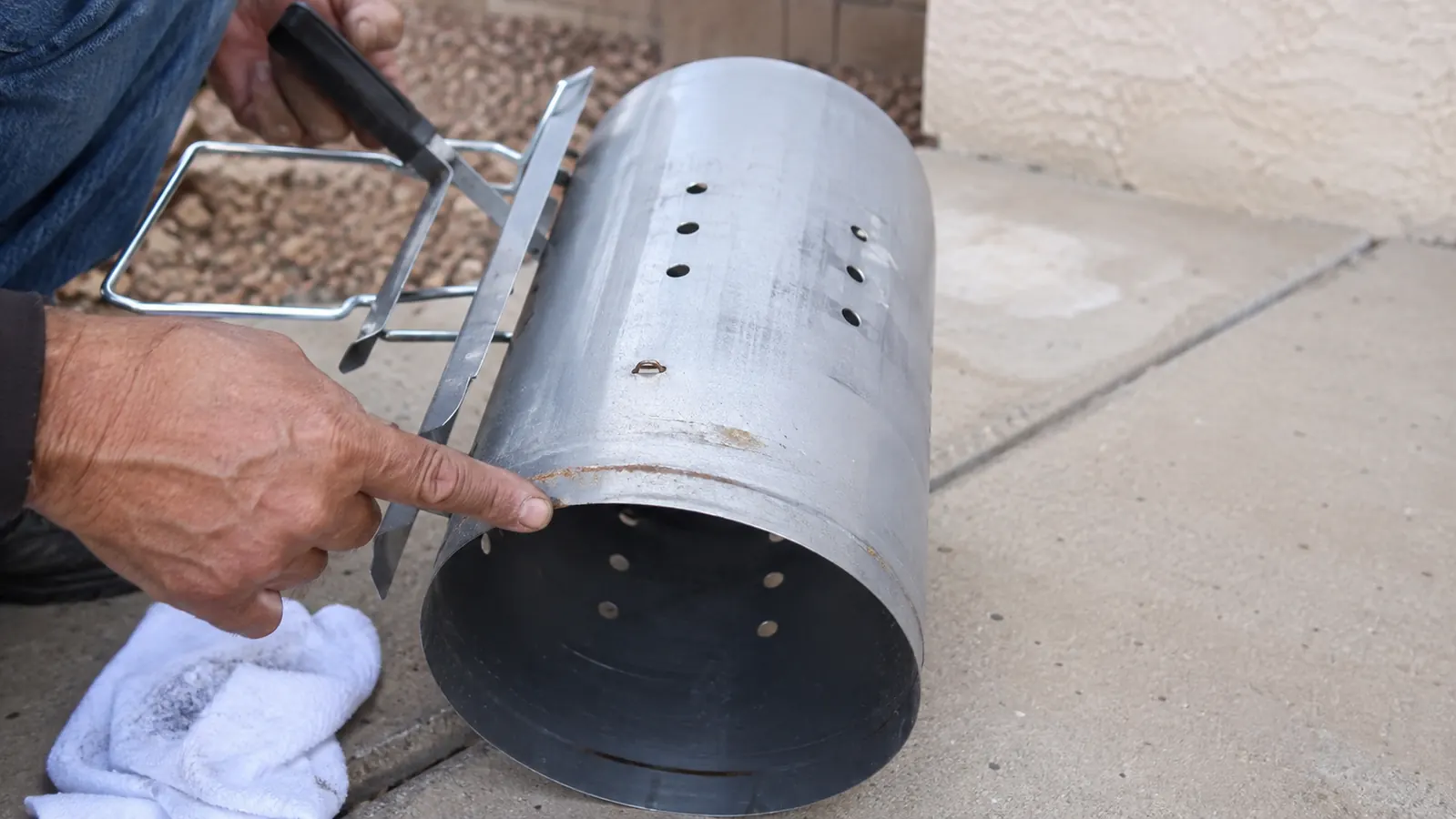 A weathered chimney starter tipped on its side revealing a faint rust line along the bottom seam where two pieces of metal meet