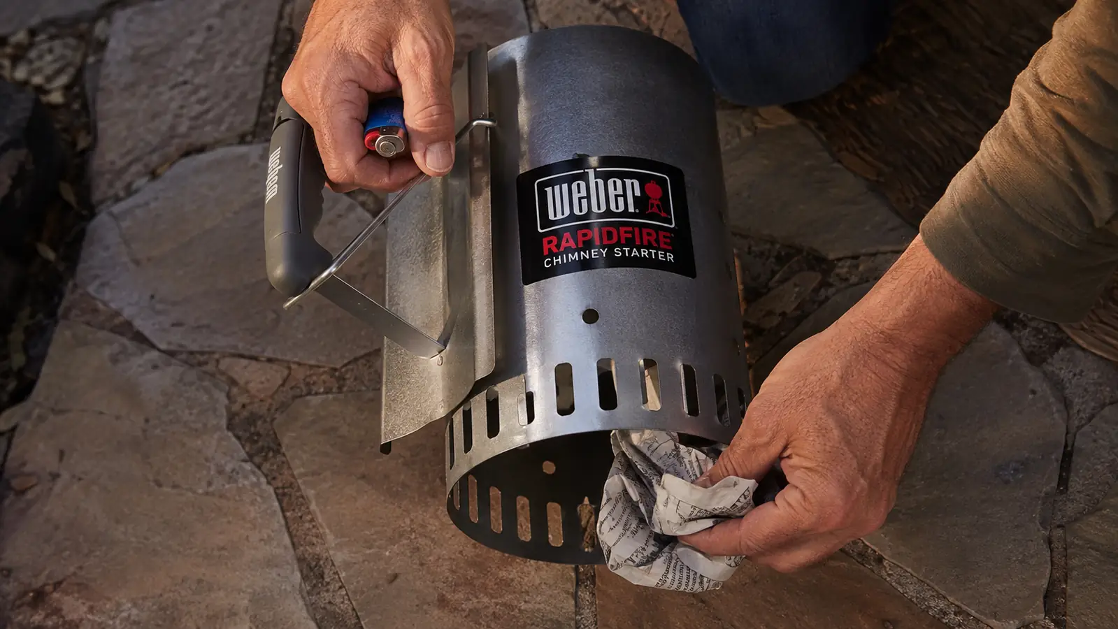 Crumpled newspaper being tucked under a chimney starter set on a patio before lighting