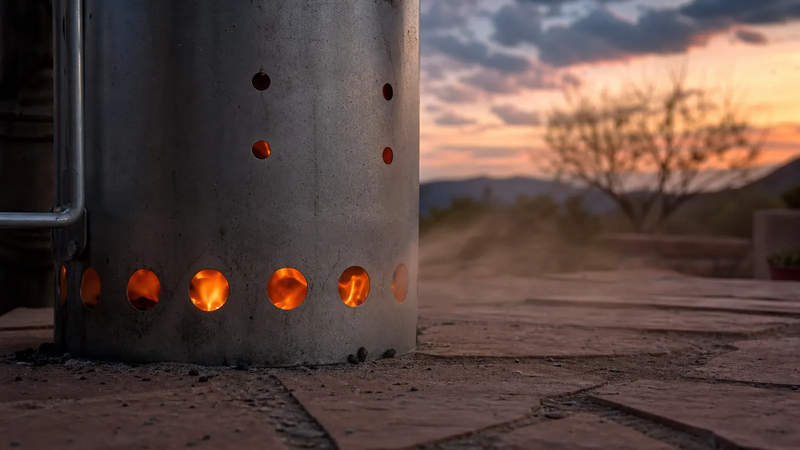 A lit chimney starter glowing through its bottom vent holes on a windy patio evening